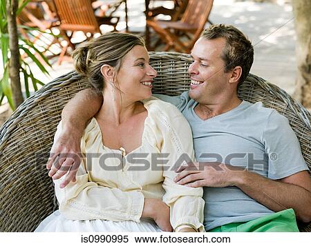 Mid adult couple sitting on wicker chair View Large Photo Image Stock Photography - Mid adult couple sitting on wicker chair. Fotosearch