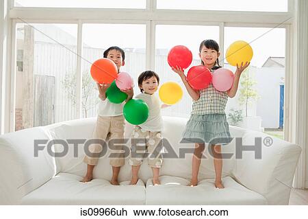 Three children standing on sofa with balloons View Large Photo Image Stock Image - Three children standing on sofa with balloons. Fotosearch