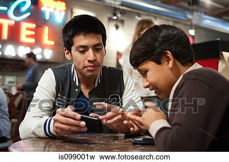 Stock Photo - Two brothers with smartphone in cafe. Fotosearch