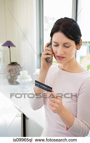 Stock Image - Woman home shopping on phone with credit card. Fotosearch