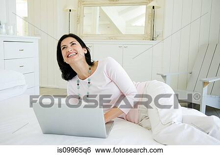 Woman lying on bed using laptop View Large Photo Image Stock Photograph - Woman lying on bed using laptop. Fotosearch