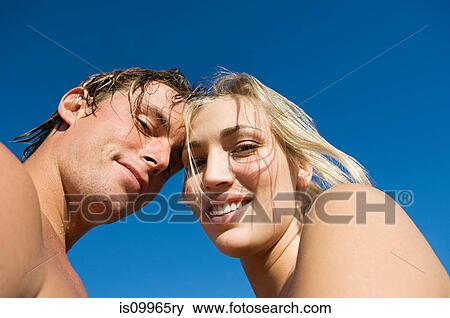 Stock Photo - Young couple looking at camera against blue sky. Fotosearch