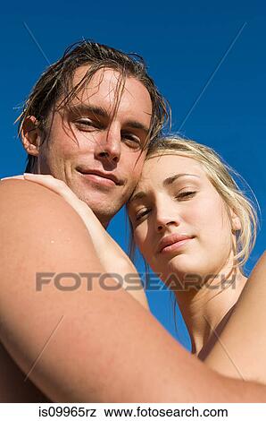 Young couple looking at camera against blue sky View Large Photo Image Stock Photo - Young couple looking at camera against blue sky. Fotosearch