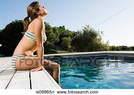 Stock Photography - Young woman sitting at poolside. Fotosearch