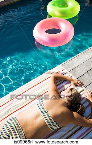 Young woman sunbathing at poolside View Large Photo Image Stock Image - Young woman sunbathing at poolside. Fotosearch