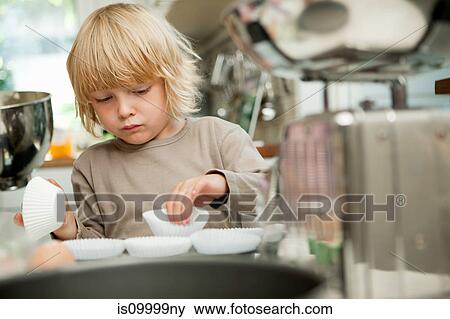 Stock Photo - Boy arranging cake cases on baking tray. Fotosearch