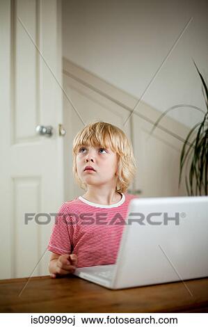 Boy looking up from laptop on desk View Large Photo Image Stock Image - Boy looking up from laptop on desk. Fotosearch