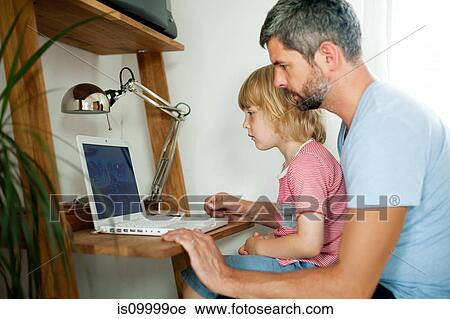 Boy sitting on father's lap at computer desk View Large Photo Image Stock Image - Boy sitting on father's lap at computer desk. Fotosearch
