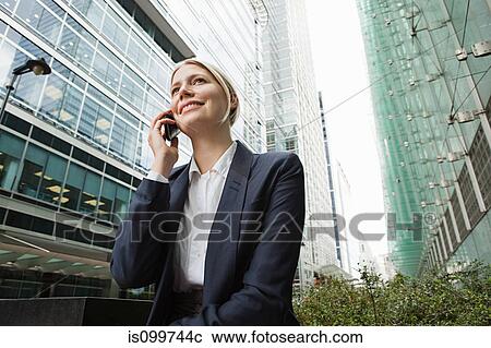 Stock Image - Businesswoman on cellphone amongst office buildings. Fotosearch