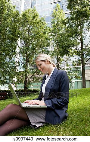 Businesswoman sitting on grass and using laptop View Large Photo Image Stock Photo - Businesswoman sitting on grass and using laptop. Fotosearch