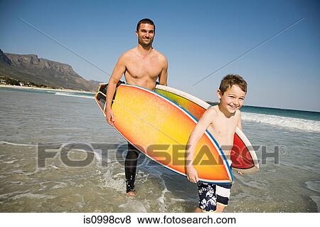 Father and son carrying surfboards in from the sea View Large Photo Image Stock Photo - Father and son carrying surfboards in from the sea. Fotosearch