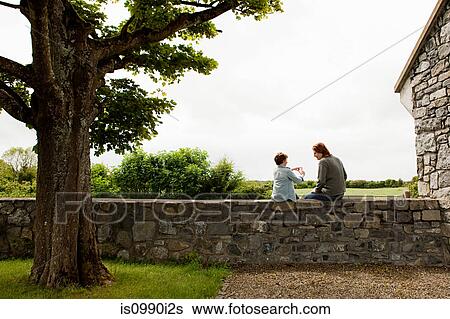 Father and son sitting on stone wall View Large Photo Image Stock Photograph - Father and son sitting on stone wall. Fotosearch