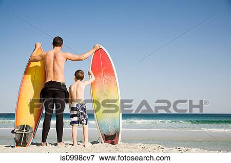 Father and son with surfboards gazing out to sea View Large Photo Image Stock Photo - Father and son with surfboards gazing out to sea. Fotosearch