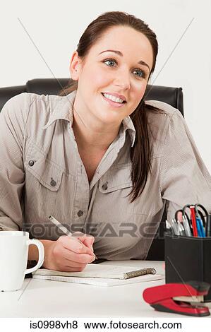 Female worker looking up after writing in a notebook View Large Photo Image Stock Photo - Female worker looking up after writing in a notebook. Fotosearch