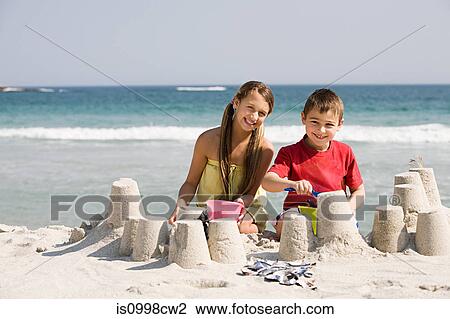Stock Image - Girl and boy making sandcastles on the beach. Fotosearch