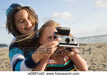 Girl showing friend how to use instant camera at beach View Large Photo Image Stock Image - Girl showing friend how to use instant camera at beach. Fotosearch