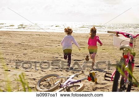 Stock Image - Girls running toward sea at beach. Fotosearch