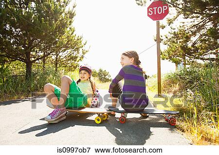 Girls sitting on skateboards along rural road View Large Photo Image Stock Photo - Girls sitting on skateboards along rural road. Fotosearch
