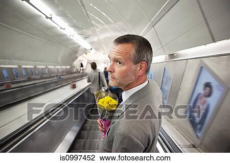 Stock Image - Man on subway escalator with flowers. Fotosearch