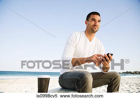 Man using mobile phone on a beach View Large Photo Image Stock Photography - Man using mobile phone on a beach. Fotosearch