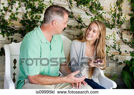 Stock Image - Mature man and daughter sitting together outside. Fotosearch