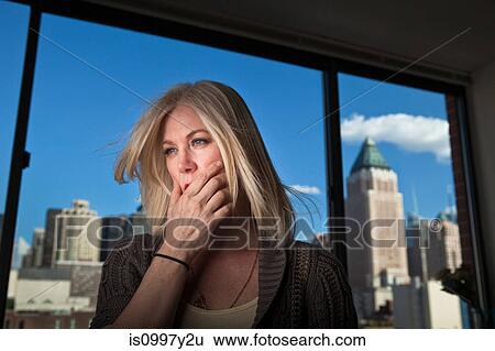 Stock Photograph - Mature woman looking anxious in office with cityscape visible behind. Fotosearch