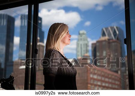 Mature woman staring out of an office block window at skyscrapers View Large Photo Image Stock Photograph - Mature woman staring out of an office block window at skyscrapers. Fotosearch