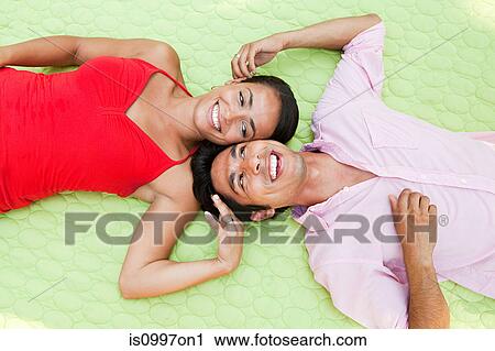 Stock Image - Mid adult couple lying on blanket outdoors, portrait. Fotosearch