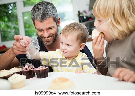 Picture - Mid adult man decorating cupcakes with his sons. Fotosearch
