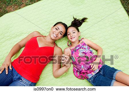 Stock Image - Mother and daughter lying on blanket, holding hands. Fotosearch