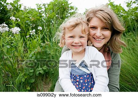 Stock Photo - Mother and daughter sitting in field, looking at camera. Fotosearch
