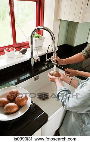 Stock Image - Mother and son washing potatoes in kitchen sink. Fotosearch