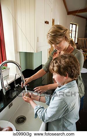 Stock Image - Mother and son washing potatoes in kitchen sink. Fotosearch