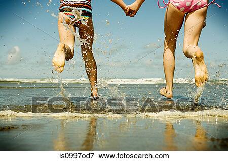 Stock Photo - Two girls holding hands running into sea. Fotosearch