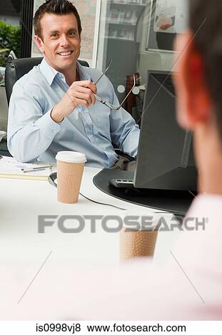 Stock Photo - Two male colleagues sitting behind their desks. Fotosearch