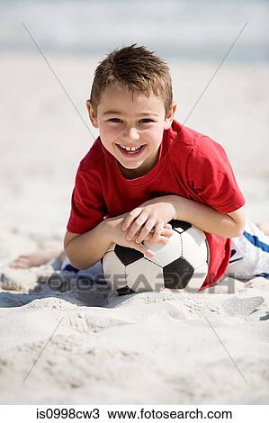Stock Image - Young boy holding football on a beach. Fotosearch