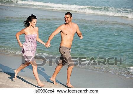 Picture - Young couple running along the water's edge on a beach. Fotosearch