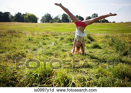 Stock Image - Young woman doing a handstand in a field. Fotosearch