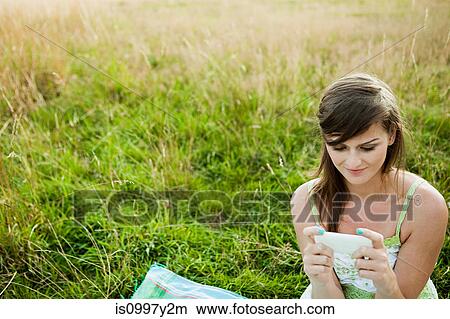 Young woman looking at a hand held device in a field View Large Photo Image Picture - Young woman looking at a hand held device in a field. Fotosearch