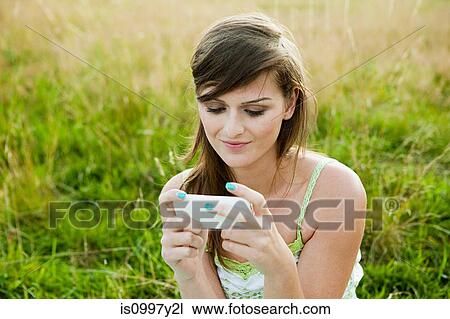 Young woman looking at a hand held device in a field View Large Photo Image Stock Image - Young woman looking at a hand held device in a field. Fotosearch