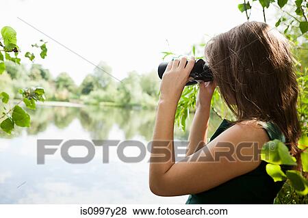 Stock Photo - Young woman looking through binoculars across a lake. Fotosearch