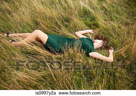 Young woman lying down in a field in a green dress View Large Photo Image Stock Image - Young woman lying down in a field in a green dress. Fotosearch