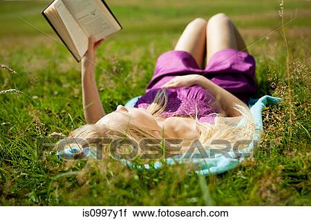 Young woman lying down reading a book in a field View Large Photo Image Stock Image - Young woman lying down reading a book in a field. Fotosearch