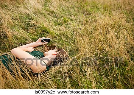 Young woman lying in a field using her mobile phone View Large Photo Image Stock Image - Young woman lying in a field using her mobile phone. Fotosearch