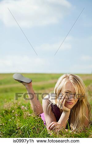 Stock Image - Young woman lying on her front in a field, smiling. Fotosearch
