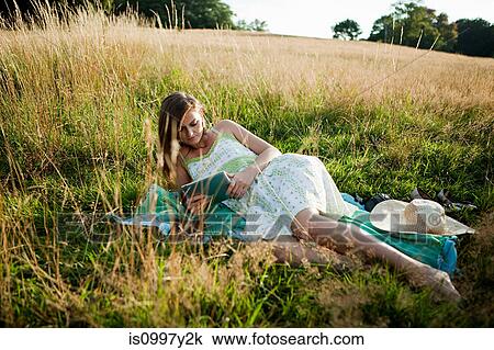 Young woman lying on side in a field looking at a hand held device View Large Photo Image Stock Image - Young woman lying on side in a field looking at a hand held device. Fotosearch
