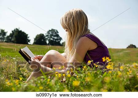 Young woman reading a book in a field View Large Photo Image Stock Image - Young woman reading a book in a field. Fotosearch