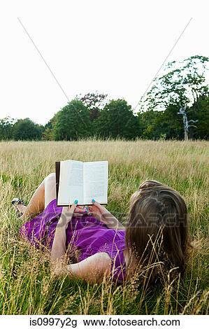 Young woman reading a book in a field View Large Photo Image Stock Image - Young woman reading a book in a field. Fotosearch