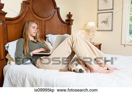 Stock Photography - Young woman relaxing on bed with laptop. Fotosearch