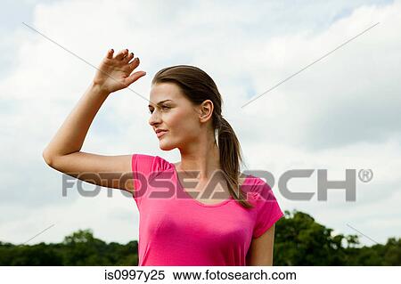 Young woman shielding eyes from the sun in the countryside View Large Photo Image Stock Photography - Young woman shielding eyes from the sun in the countryside. Fotosearch